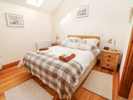 A bedroom with a bed covered in white and plaid bedding two wooden bedside tables and framed pictures on the walls at Rayson Hall Barns in Ousby