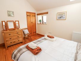 A bedroom with a bed, wooden chest of drawers with mirrors, a wooden chair, and a small window at Rayson Hall Barns in Ousby