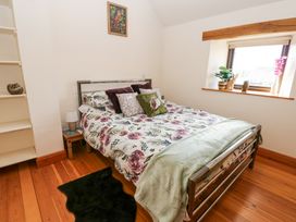 A bedroom with a floral bedspread a bedside table with a lamp and a window with plants and ornaments at Rayson Hall Barns in Ousby