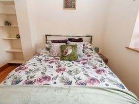 A bedroom with a bed having floral bedding and decorative pillows beside shelves and a window at Rayson Hall Barns in Ousby