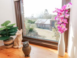A wooden windowsill with a potted plant a wooden dog statue a wooden owl statue and pink flowers in a white vase at Rayson Hall Barns in Ousby
