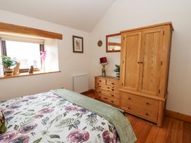 A bedroom with a bed with floral bedding wooden wardrobe and dresser by a window at Rayson Hall Barns in Ousby