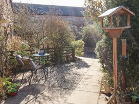 An outdoor patio area with two chairs and a small round table with glasses and a bottle surrounded by plants and a bird feeder at Rayson Hall Barns in Ousby
