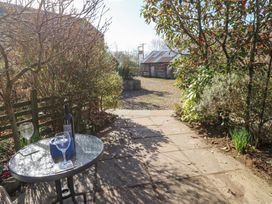 A garden patio with a small glass table holding two wine glasses and a bottle at Rayson Hall Barns in Ousby
