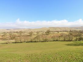 A grassy field with scattered trees and hills in the background under a blue sky at Rayson Hall Barns in Ousby