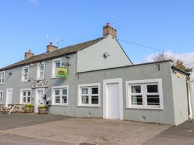 A grey building with white framed windows and doors with a sign reading The Fox Inn and outdoor benches at Rayson Hall Barns in Ousby
