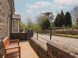 A stone patio with a wooden bench and metal railing overlooking a road and trees at 2 High Lane Terrace in Kirkby Stephen