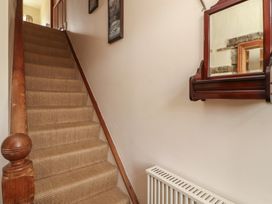 A carpeted staircase with wooden handrails and framed pictures on the wall next to a red wooden mirror above a white radiator at 2 High Lane Terrace Kirkby Stephen