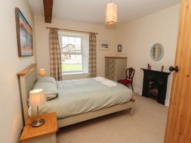 A bedroom with a bed and bedside table with lamps a window with curtains a chest of drawers a chair a small fireplace and a wooden door at 2 High Lane Terrace in Kirkby Stephen