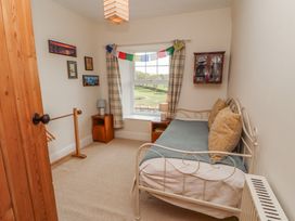 A small bedroom with a metal framed bed and pillows next to a window with curtains at 2 High Lane Terrace in Kirkby Stephen