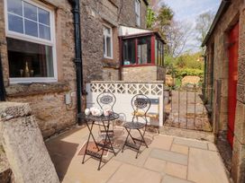 An outdoor patio with a black metal table and two chairs and a stone house wall at 2 High Lane Terrace Kirkby Stephen