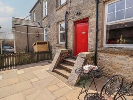 A stone patio with a black metal table and chairs and a red door at 2 High Lane Terrace in Kirkby Stephen