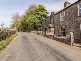 A paved road running alongside stone houses and stone walls with trees in the background at 2 High Lane Terrace in Kirkby Stephen