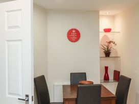 A dining area with a wooden table and four chairs a red wall clock and glass shelves with decorative items at Counting House in Bridlington