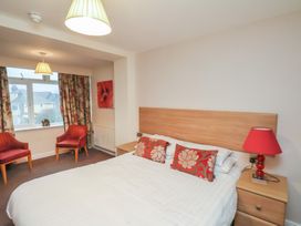 A bedroom with a double bed with patterned pillows two armchairs by a window a bedside table with a red lamp and a painting on the wall at Counting House in Bridlington