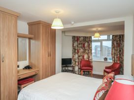 A bedroom with a bed two red chairs a window with curtains wooden wardrobes and a small desk at Counting House in Bridlington