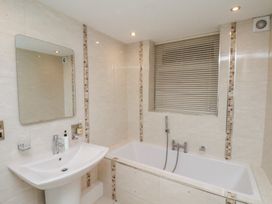 A bathroom with a sink pedestal mirror bathtub window with blinds and tiled walls at Counting House in Bridlington