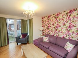 A living room with a purple sofa, armchair, wooden coffee table, floral wallpaper, green curtains, and a chandelier at Secret Garden in Bridlington