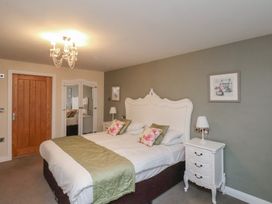 A bedroom with a double bed with floral pillows and green runner two white bedside tables a wooden door and a mirrored wardrobe at Secret Garden in Bridlington