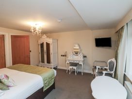 A bedroom with a bed green bedspread wardrobe dressing table chairs and a wall-mounted tv at Secret Garden in Bridlington