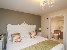 A bedroom with a large white headboard beige floral pillows green bed runner and an attached bathroom at Secret Garden in Bridlington