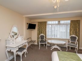 A room with a vanity table and chair a wall-mounted TV two armchairs a table and a window with curtains at Secret Garden in Bridlington