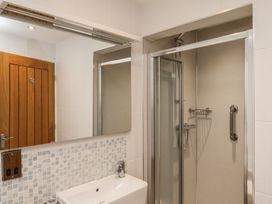 A bathroom with a sink and mirror next to a shower cubicle with a sliding door and wooden door at Secret Garden in Bridlington