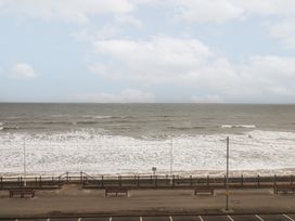 A sea view with waves hitting a beach and benches along a promenade at Lookout Post in Bridlington