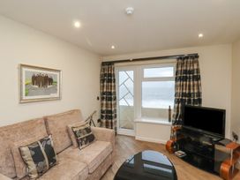 A living room with a beige sofa cushions a painting a black TV on stand wooden floor and a window with curtains showing ocean view at Lookout Post in Bridlington