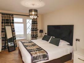 A bedroom with a double bed black and beige curtains a standing mirror and a bedside lamp at Lookout Post in Bridlington
