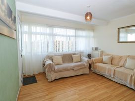 A living room with two sofas covered in throws a large window with vertical blinds and sheer curtains a green wall with a beach picture and a wooden floor at Chalet 469 Newport Norfolk