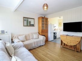 A living room with two sofas a wooden cabinet a wall-mounted TV and an open doorway to a kitchen at Chalet 469 in Newport Norfolk