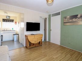 A room with a wall-mounted television above a wooden folding table and a view into a kitchen area at Chalet 469 in Newport Norfolk