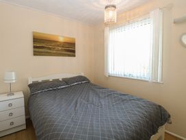 A bedroom with a double bed covered in gray checkered bedding a white bedside table with a lamp and a window with white curtains at Chalet 469 in Newport Norfolk