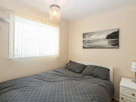 A bedroom with a bed with checkered bedding a window with sheer curtains a nightstand with a lamp and a seascape picture on the wall at Chalet 469 in Newport Norfolk