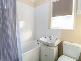 A bathroom with a bathtub and shower curtain a sink with hand soap and a toilet at Chalet 469 in Newport Norfolk