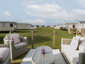 An outdoor seating area with wicker furniture and cushions overlooking a grassy area with caravans at Breathing Space Happisburgh near Walcott