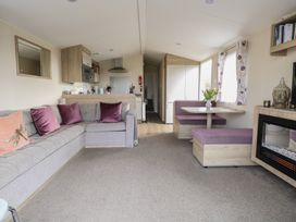 A living area with a grey sofa with purple pillows a dining nook with purple seating a kitchen area and a wall-mounted electric fireplace at Breathing Space in Happisburgh near Walcott