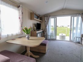 A living area with a wooden table and pink seating a television a bookshelf and sliding glass doors opening to a lawn at Breathing Space in Happisburgh near Walcott
