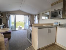 An open plan living area with kitchen cabinets a microwave a toaster a dining table with chairs and a sofa in Breathing Space Happisburgh near Walcott