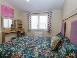 A bedroom with a patterned bedspread a window with curtains and a wooden dressing table with a statue at Breathing Space in Happisburgh near Walcott