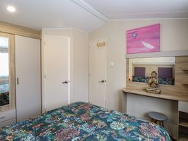 A bedroom with a floral bedspread a wardrobe two doors a dressing table with a Buddha statue and a pink painting on the wall at Breathing Space in Happisburgh near Walcott