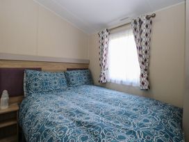 A bedroom with a double bed a bedside table and a window with patterned curtains at Breathing Space in Happisburgh near Walcott