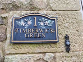 A house number plaque with floral decoration and the name Timberwick Green mounted on a stone wall at Timberwick Green Akeld near Wooler