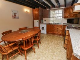 A kitchen with wooden cabinets a washing machine dining table and chairs with a window above the sink at Timberwick Green in Akeld near Wooler