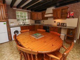 A kitchen with wooden cabinets a round wooden table and chairs a washing machine and appliances at Timberwick Green in Akeld near Wooler
