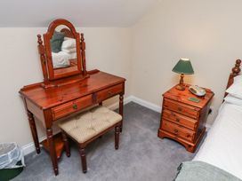 A wooden dressing table with a mirror and cushioned stool next to a wooden bedside table with a lamp and clock radio in a bedroom at Timberwick Green in Akeld near Wooler
