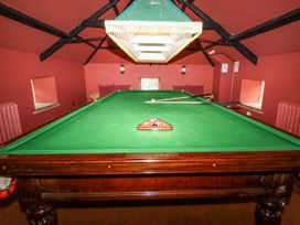 A snooker table with a green lamp above and two cues resting on the table in a room with red walls
