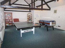 A game room with a ping pong table foosball table bookshelves and a chair at Timberwick Green in Akeld near Wooler