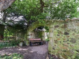 A wooden bench under a stone arch in a garden with a stone wall and trees at Timberwick Green in Akeld near Wooler